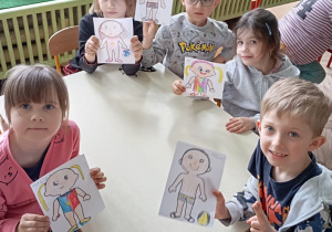 Dzieci przy stole prezentują swoje rysunki