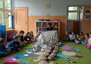 dzieci siedzą w kole, na środku dywanu leżą fantomy