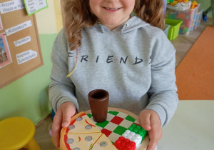 uśmiechnięta dziewczynka trzyma tacę z zabawkową pizzą ii kawą