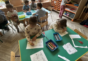 dzieci siedzą przy stolikach i kolorują obrazek