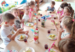 dzieci przy stole jedzą sałatkę owocową
