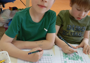 Chłopcy zamalowują określone pola na kartce