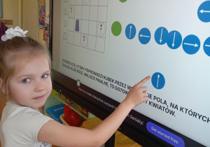 dziewczynka przy tablicy interaktywnej wyciąga palec wskazujący