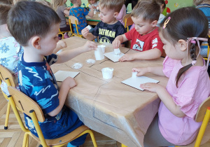 dzieci siedzą przy stoliku i wykonują upominki dla mamy i taty