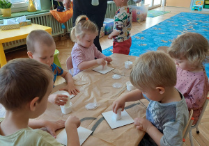 dzieci siedzą przy stoliku i wykonują upominki dla mamy i taty