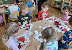 dzieci siedzą przy stoliku i wykonują upominki dla mamy i taty