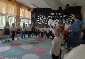 grupa dzieci ubrana na galowo w półkolu z Panią Dyrektor i nauczycielem