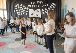 grupa dzieci w półkolu a jedna z dziewczynek podchodzi do nauczycielek