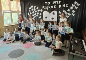 grupa dzieci z książkami pozują do zdjęcia z nauczycielami na tle dekoracji z motylami