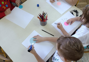 dzieci siedzą przy stoliku i wykonują prace plastyczną
