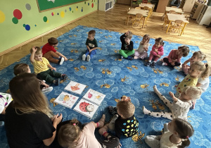 dzieci siedzą w kole, na dywanie leżą cztery obrazki