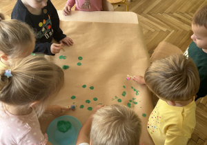 dzieci siedzą przy stoliku i stemplują farbą kropki