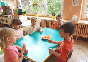 dzieci siedzą przy stoliku i jedzą marchewki
