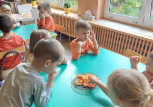 dzieci siedzą przy stoliku i jedzą marchewki