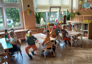 dzieci siedzą przy stoliku i trzymają kubeczki w ręku