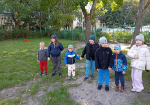 dzieci stoją na trawie w ogrodzie przedszkolnym i trzymają się za ręce