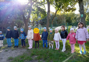 dzieci stoją na trawie w ogrodzie przedszkolnym i trzymają się za ręce