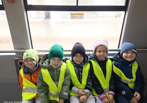 pięcioro dzieci w kamizelkach odblaskowych siedzi w tramwaju
