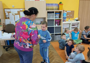 chłopiec stoi przed panią a za nim reszta dzieci siedząca na dywanie