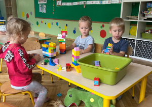 dzieci siedzą przy stoliku i budują budowle z klocków