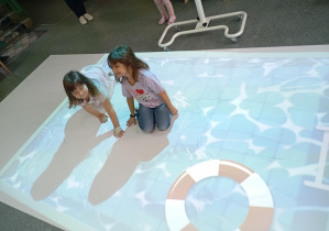 dwie dziewczynki siedzą na macie interaktywnej