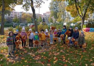 grupa dzieci ustawione w szeregu z bukietami liści w ogrodzie