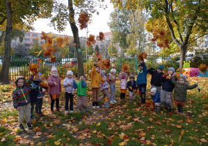 Dzieci podrzucają kolorowe liście w ogrodzie