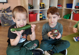 jeden chłopiec trzyma w rękach ogórka a drugi słoik z ogórkami