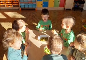 dzieci siedzą przy stoliku i jedzą ogórki