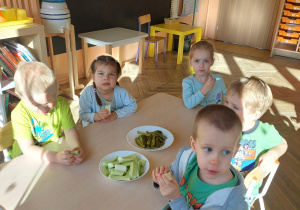 dzieci siedzą przy stoliku i jedzą ogórki
