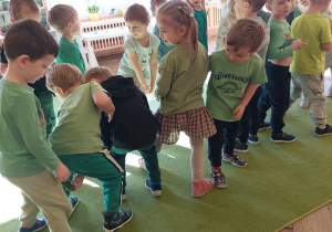 dzieci stoją w dwóch rzędach i podają sobie ogórka między nogami