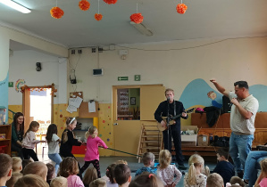 na scenie kilkoro dzieci trzyma długą linę a z drugiej strony stoi prowadzący i wokalista z gitarą