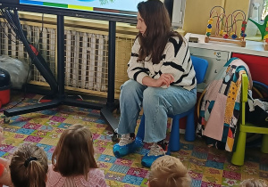 pani prowadząca siedzi na krzesełku a obok niej ekran multimedialny z obrazkiem planety Ziemia