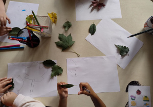 białe kartki na stole z okazami liści i rękoma dzieci