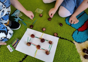 kartka z kasztanami i patyczkami oraz ręce dzieci