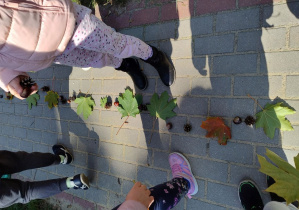 rytmiczny szereg z liści kasztanów i szyszek oraz nogi dzieci