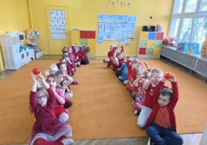 dzieci siedzące w dwóch rzędach i podające sobie piłeczki