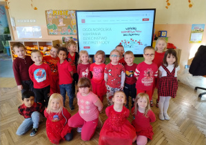 dzieci ubrane na czerwono a z tyłu ekran z projekcją kampanii Dzieciństwo bez przemocy