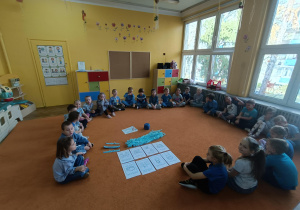 Grupa dzieci siedząca w kole z obrazkami na środku i bibułą niebieską