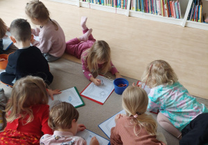dzieci siedzą na dywanie i kolorują kredkami kolorowankę