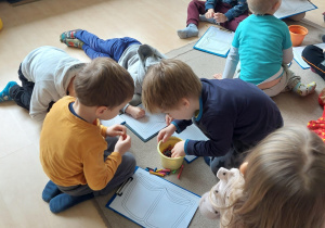 dzieci siedzą na dywanie i kolorują kredkami kolorowankę