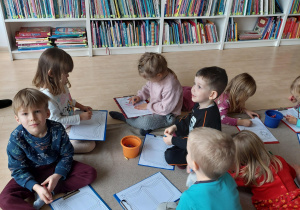 dzieci siedzą na dywanie i kolorują kredkami kolorowankę