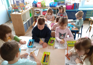 dzieci siedzą przy stolikach i kolorują kolorowanki