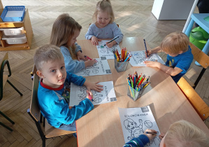 dzieci siedzą przy stolikach i kolorują kolorowanki
