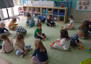 dzieci siedzą na dywanie, przed nimi leżą ułożone z kolorowych klocków rzędy