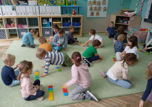 dzieci siedzą na dywanie, przed nimi leżą ułożone z kolorowych klocków rzędy