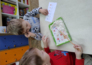chłopiec pędzelkiem odgarnia mąkę a drugi obserwuje i notuje