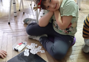 dziewczynka siedzi na podłodze. Przed nią na podłodze leży czarna mata z literkami
