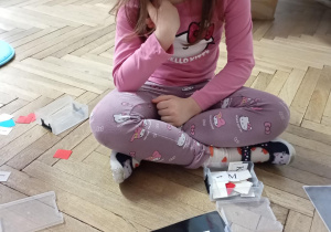 dziewczynka siedzi na podłodze. Przed nią na podłodze le