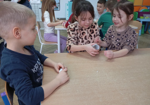 dzieci siedzą przy stolikach, trzymają w ręce rolkę po papierze